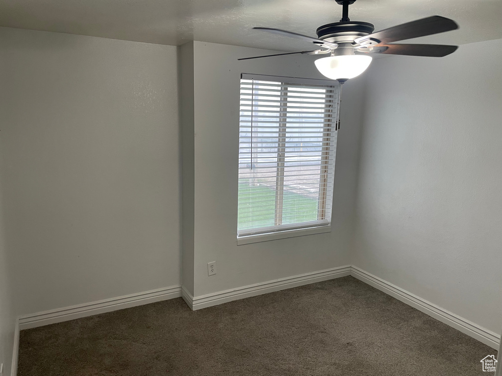 Spare room featuring baseboards, dark carpet, and ceiling fan