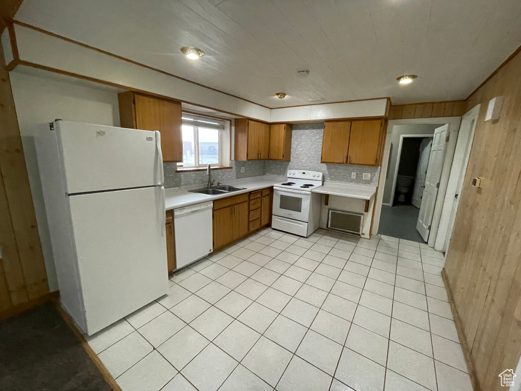 Kitchen featuring white appliances, brown cabinetry, light countertops, a sink, and wooden walls
