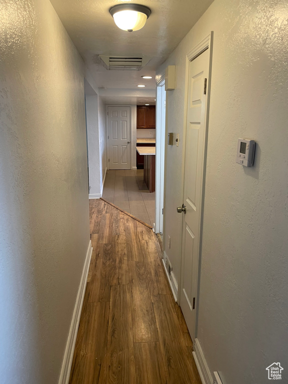Hallway featuring dark wood-type flooring, a textured wall, and baseboards