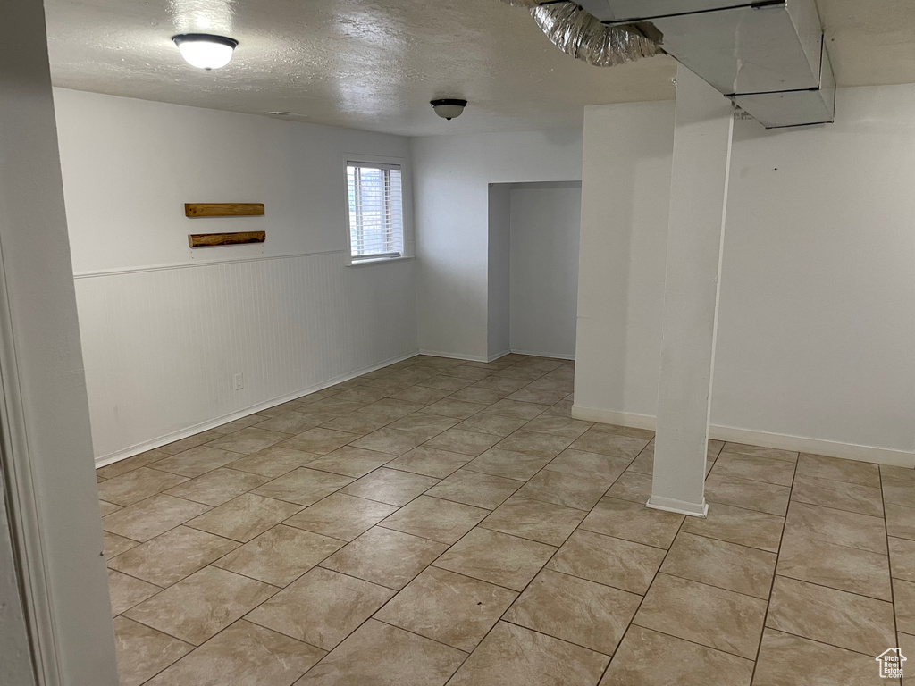 Basement with a wainscoted wall, light tile patterned flooring, and a textured ceiling