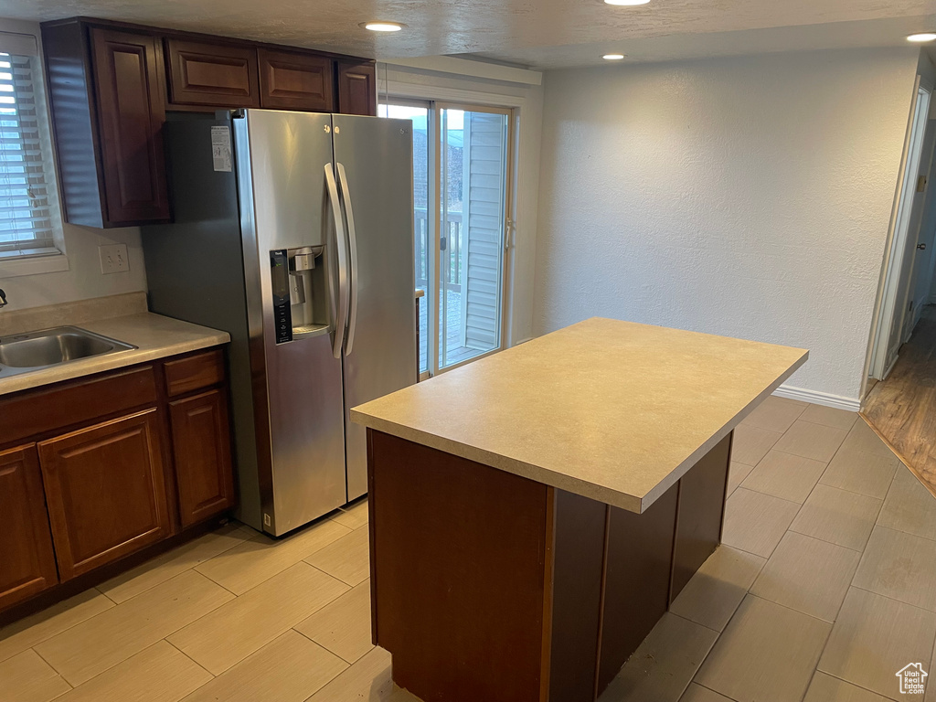Kitchen featuring wood finish floors, a kitchen island, light countertops, a sink, and stainless steel fridge