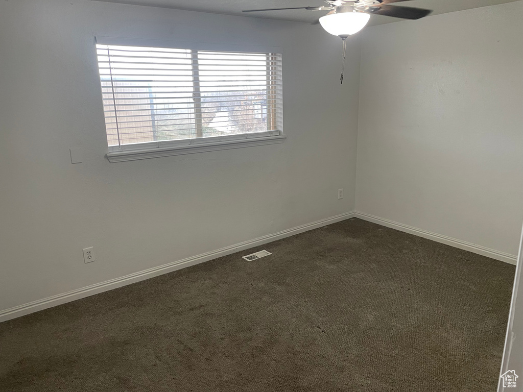 Empty room featuring visible vents, baseboards, dark carpet, and ceiling fan