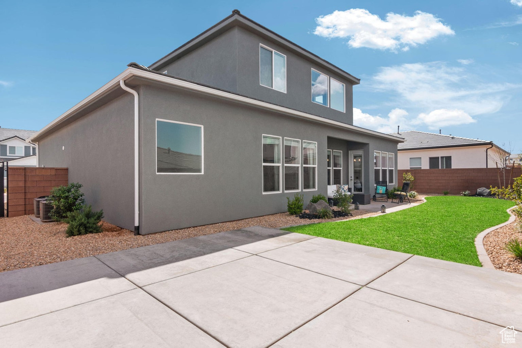 Back of house featuring stucco siding, fence, central AC unit, a patio area, and a lawn