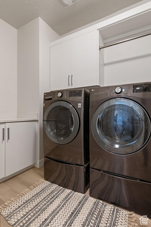 Clothes washing area with independent washer and dryer, cabinet space, and light wood-type flooring
