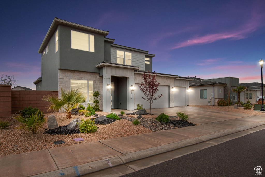Contemporary home featuring driveway, stone siding, stucco siding, fence, and an attached garage