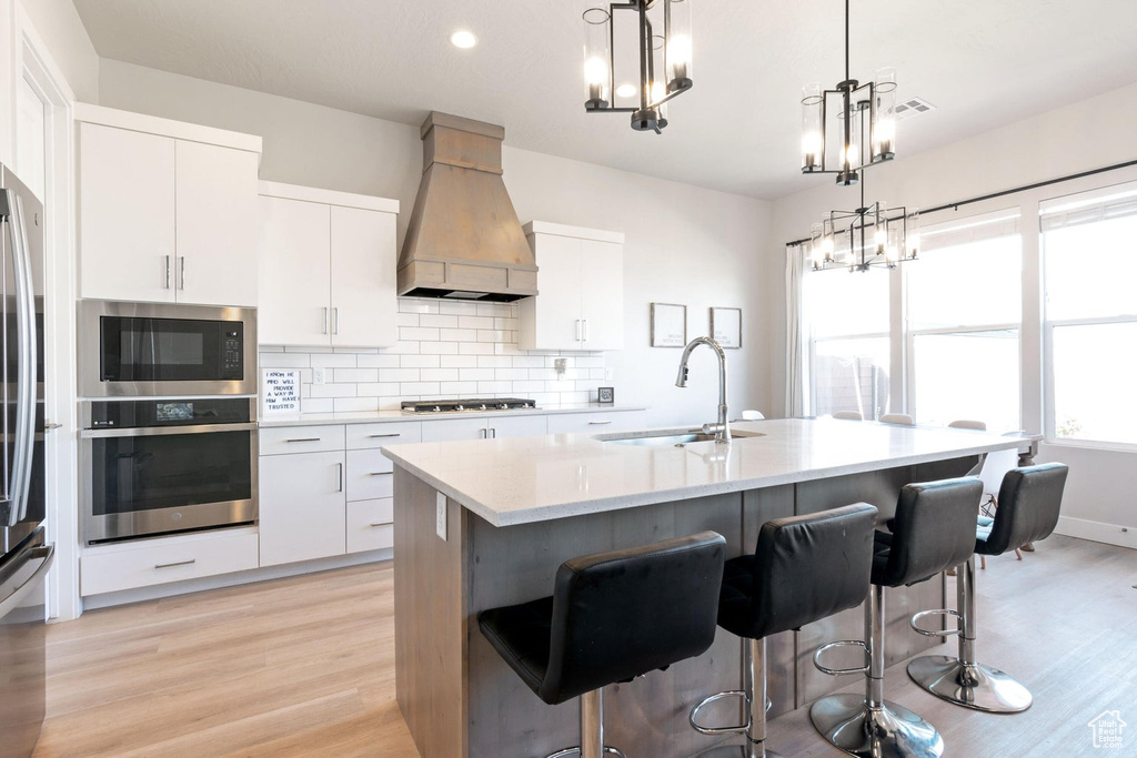 Kitchen with custom range hood, a chandelier, backsplash, a sink, and appliances with stainless steel finishes