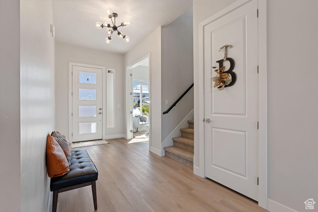 Foyer featuring baseboards, light wood-style flooring, stairway, and an inviting chandelier