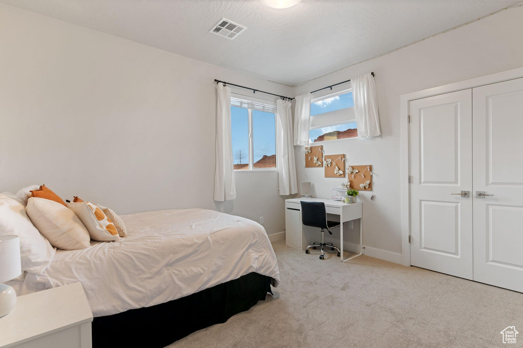 Bedroom with light carpet, baseboards, visible vents, and a closet
