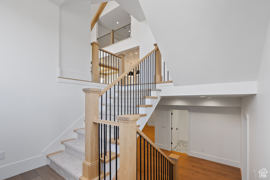 Staircase with baseboards, wood finished floors, and a towering ceiling