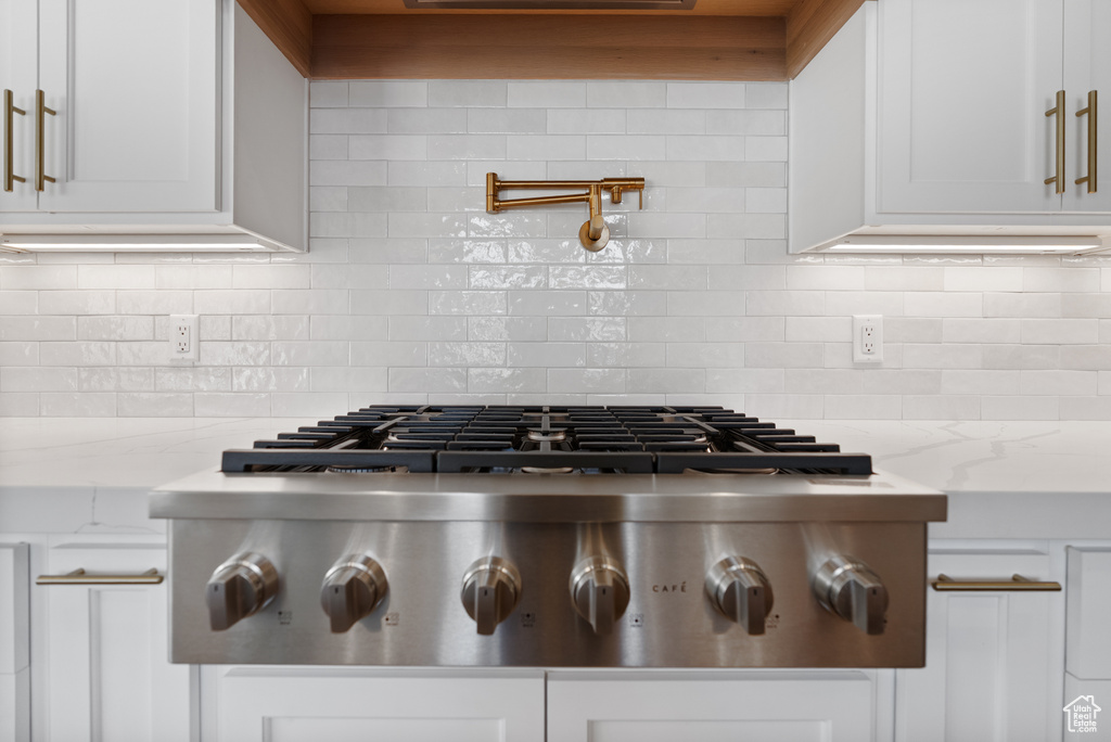 Room details with stainless steel gas stovetop, white cabinets, and backsplash