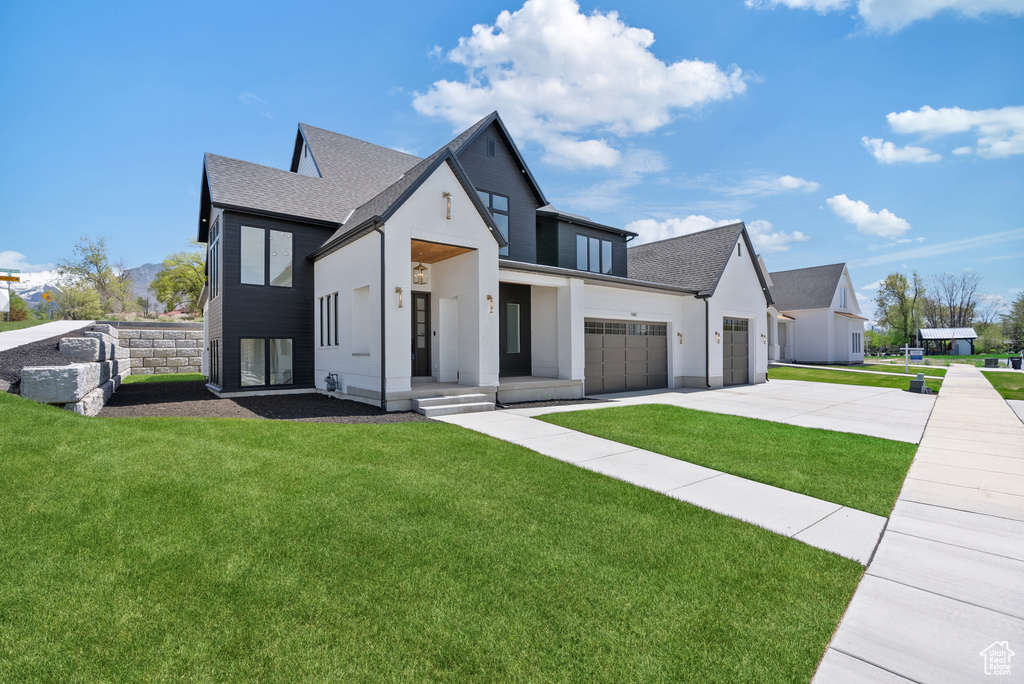 Modern farmhouse featuring a garage, concrete driveway, roof with shingles, and a front yard