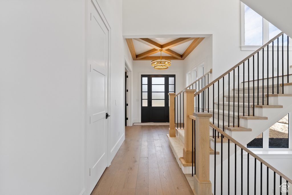 Entryway with beamed ceiling, light wood-style floors, stairway, a chandelier, and coffered ceiling