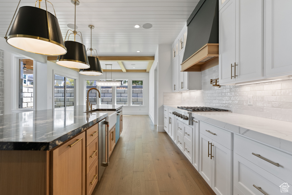 Kitchen featuring premium range hood, light wood-type flooring, light stone counters, a sink, and backsplash