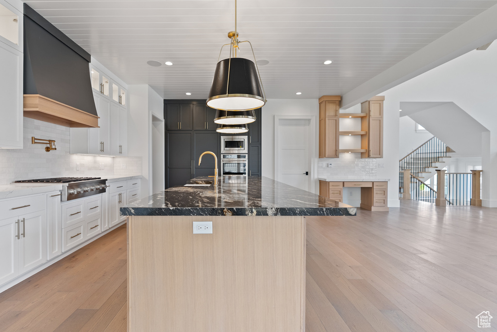 Kitchen with a sink, light wood-style flooring, premium range hood, stainless steel appliances, and decorative backsplash