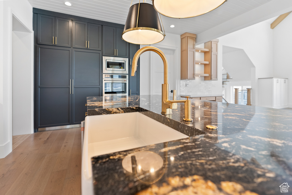 Kitchen featuring appliances with stainless steel finishes, tasteful backsplash, light wood-type flooring, a sink, and dark stone counters