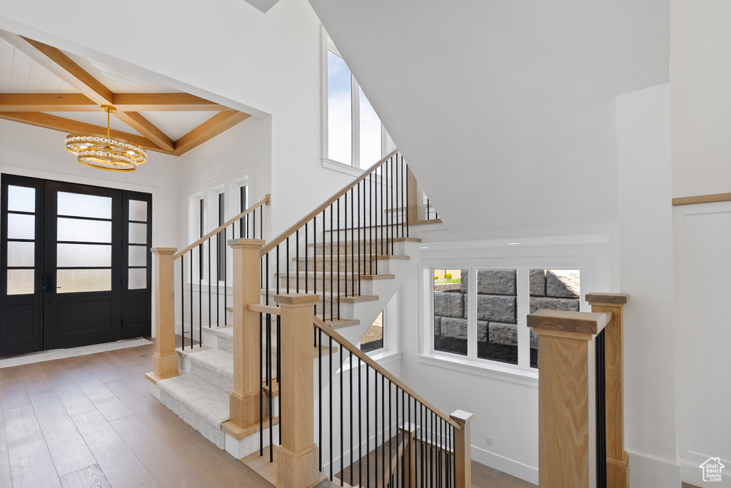 Staircase with a notable chandelier, beam ceiling, wood finished floors, a towering ceiling, and coffered ceiling
