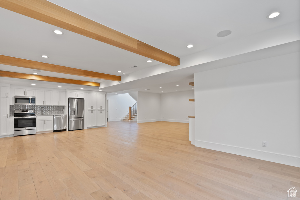 Unfurnished living room featuring recessed lighting, baseboards, light wood-type flooring, beamed ceiling, and stairway
