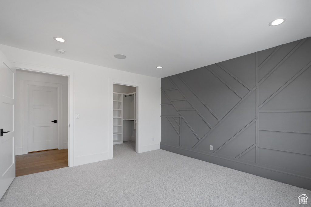 Unfurnished bedroom featuring a decorative wall, baseboards, recessed lighting, a spacious closet, and carpet