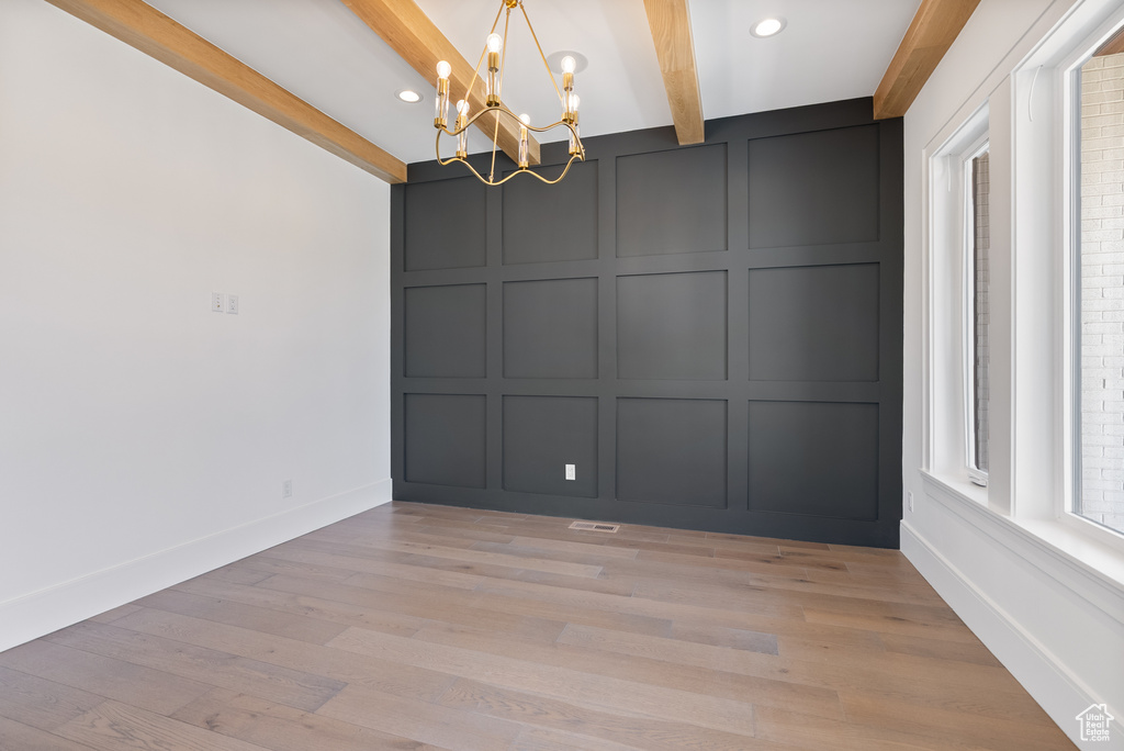 Spare room with an inviting chandelier, a decorative wall, beam ceiling, baseboards, and light wood-style floors