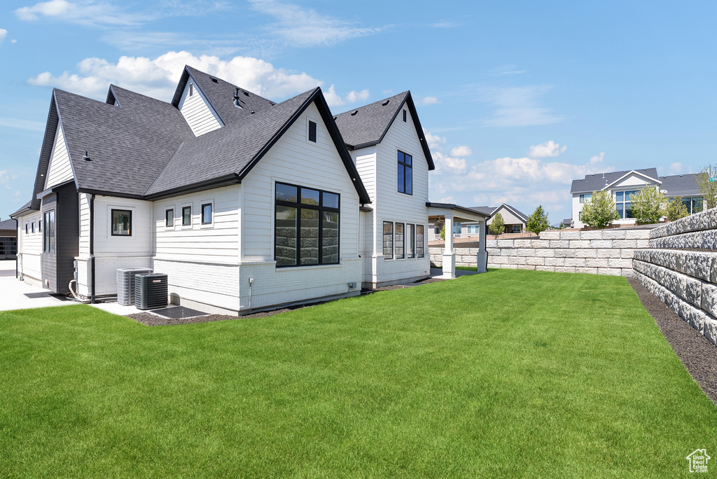 Back of house featuring a lawn, a shingled roof, a fenced backyard, and central AC unit