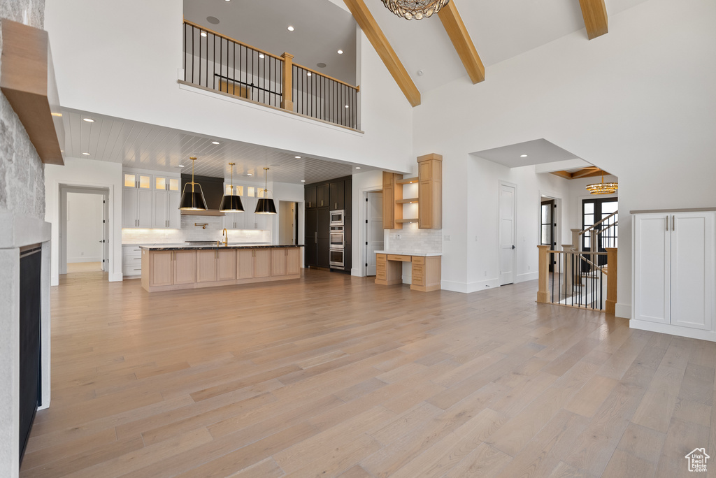 Unfurnished living room featuring beam ceiling, light wood-style floors, baseboards, high vaulted ceiling, and a chandelier