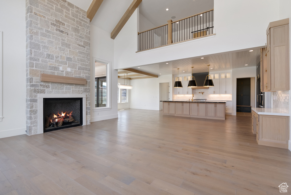 Unfurnished living room with light wood finished floors, a stone fireplace, baseboards, a towering ceiling, and beamed ceiling