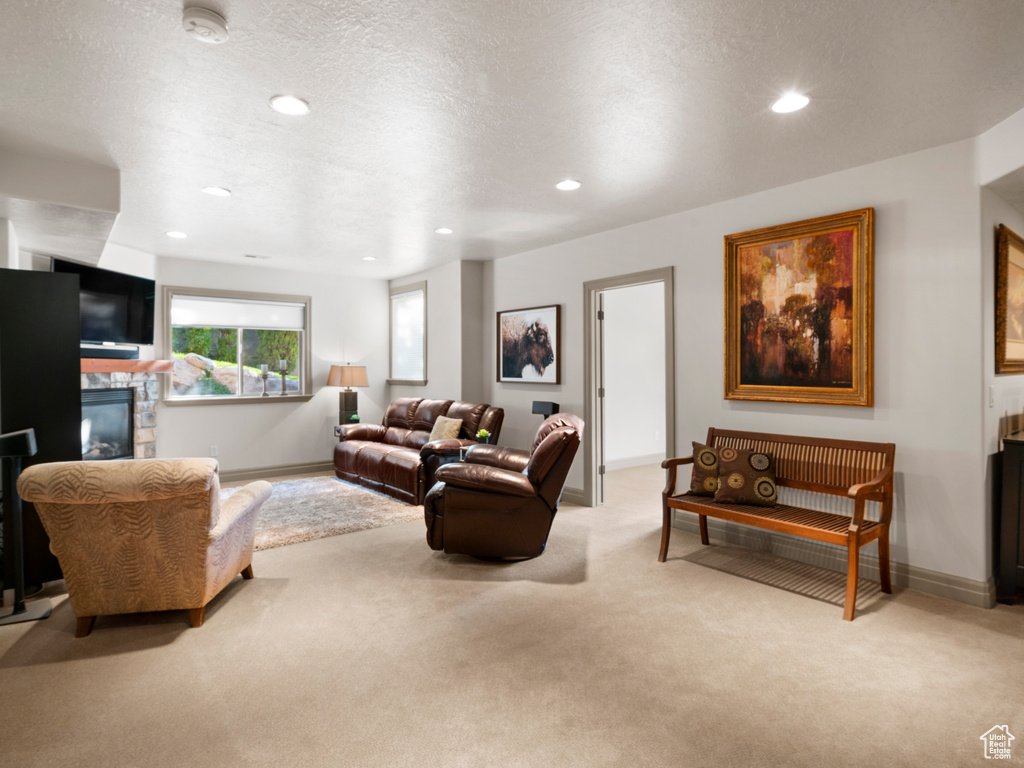 Living area featuring a textured ceiling, a stone fireplace, recessed lighting, carpet flooring, and baseboards
