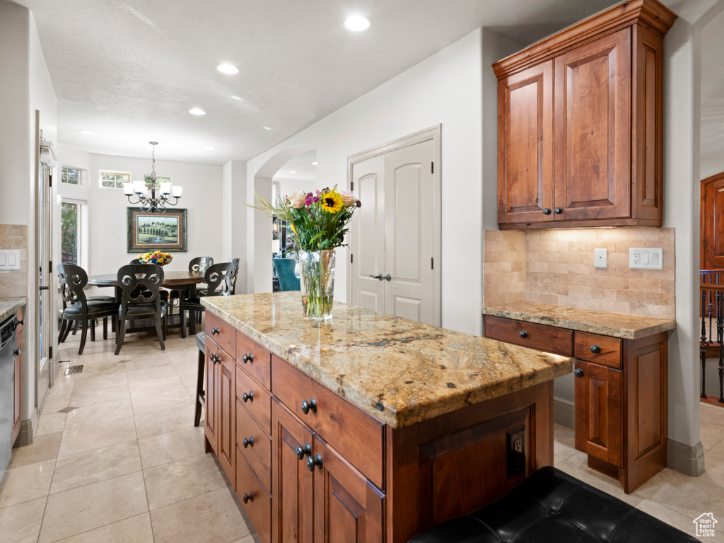 Kitchen with light stone countertops, tasteful backsplash, brown cabinets, and an inviting chandelier