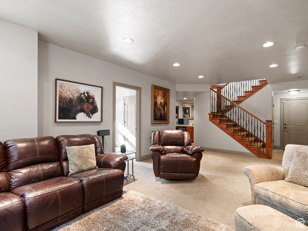 Living room featuring baseboards, a textured ceiling, light colored carpet, and stairs