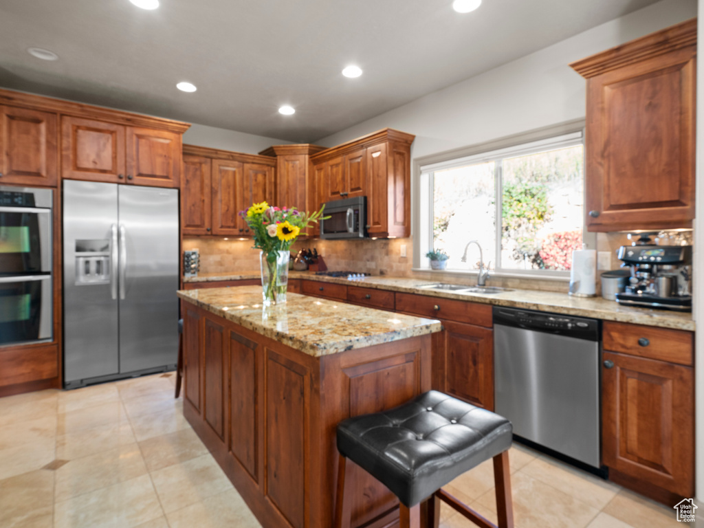 Kitchen with a center island, appliances with stainless steel finishes, light stone counters, a sink, and backsplash