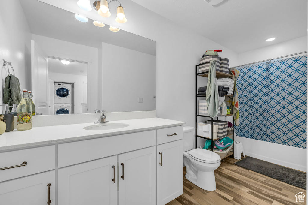 Bathroom with toilet, stacked washer and dryer, wood finished floors, and vanity