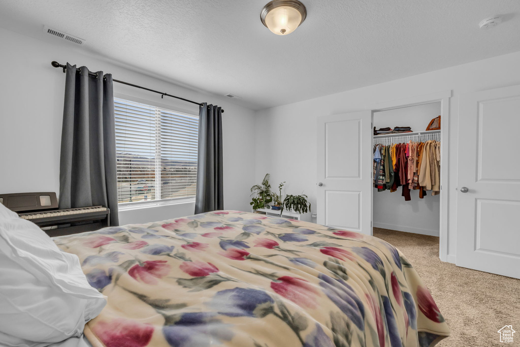Carpeted bedroom featuring a textured ceiling, a closet, visible vents, a walk in closet, and baseboards