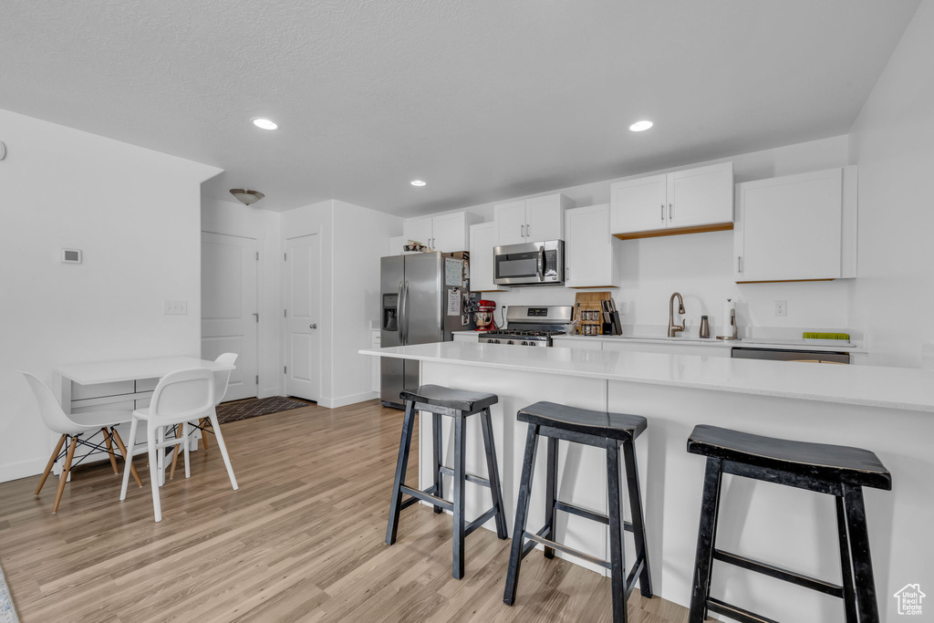 Kitchen featuring white cabinets, light countertops, light wood-type flooring, appliances with stainless steel finishes, and a breakfast bar area