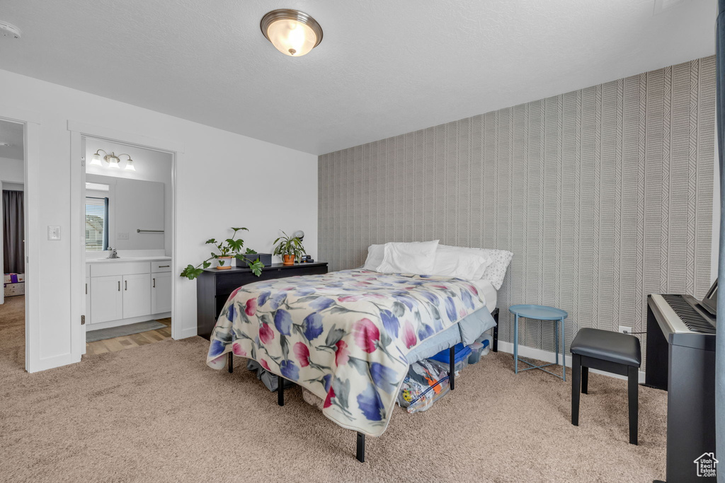 Bedroom with wallpapered walls, ensuite bath, light colored carpet, and baseboards