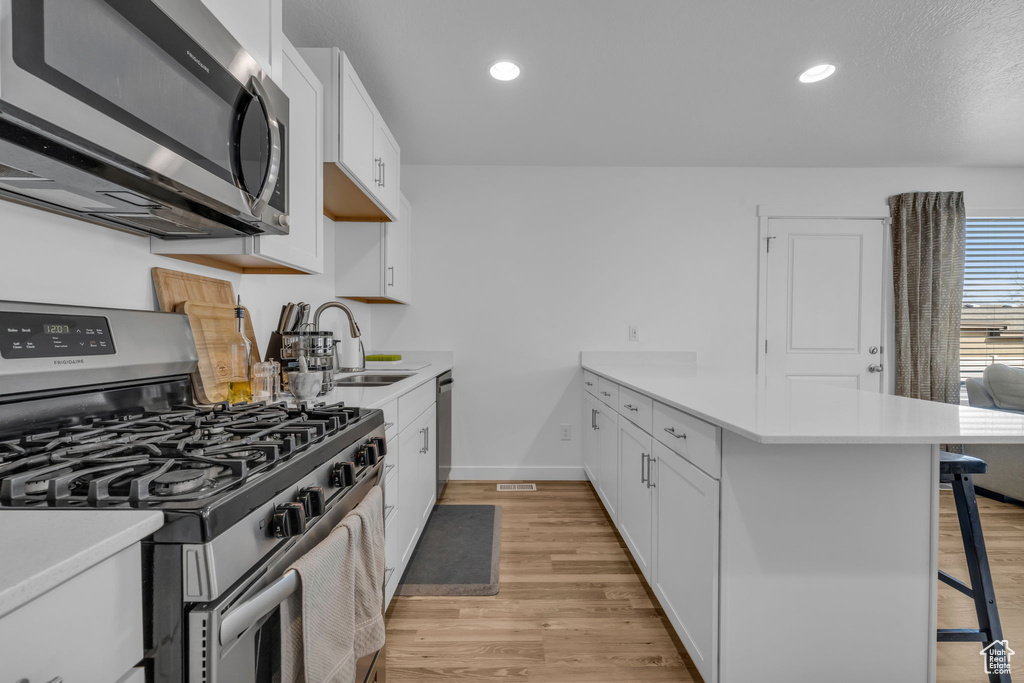 Kitchen featuring a sink, appliances with stainless steel finishes, a breakfast bar, a peninsula, and white cabinetry