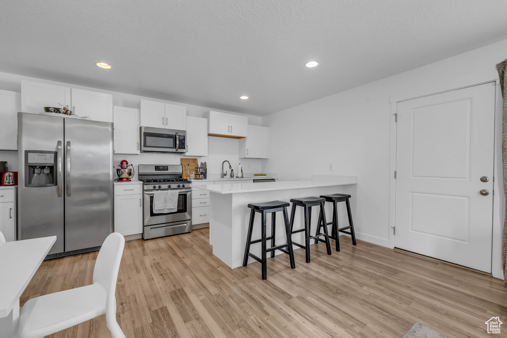 Kitchen featuring a kitchen bar, light wood-style floors, appliances with stainless steel finishes, and light countertops