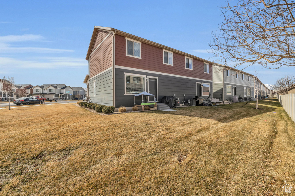Rear view of property featuring a yard, fence, cooling unit, and a residential view