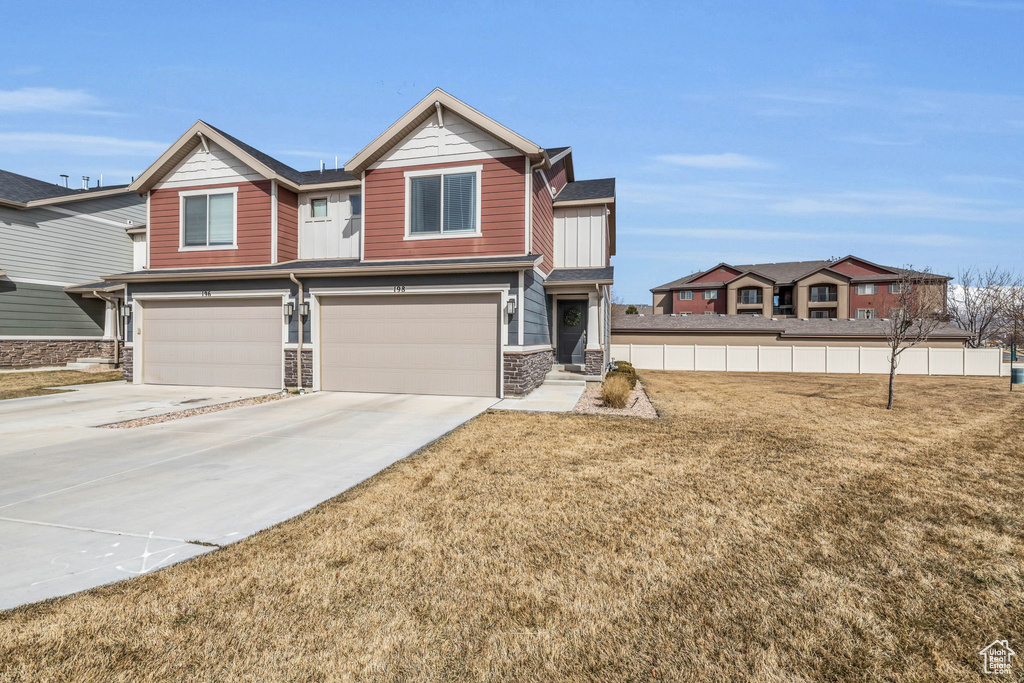 View of front facade with an attached garage, concrete driveway, a front yard, and stone siding