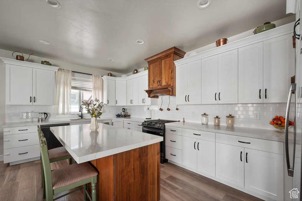 Kitchen featuring gas range, light countertops, a kitchen bar, white cabinetry, and wood finished floors