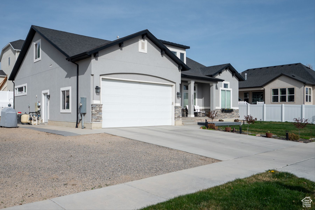 View of front of property featuring stucco siding, fence, stone siding, an attached garage, and concrete driveway