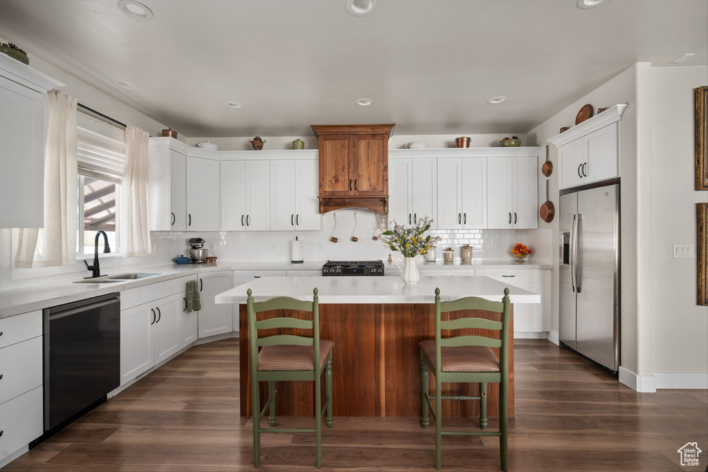 Kitchen featuring dishwasher, light countertops, a sink, stainless steel fridge, and dark wood-style flooring
