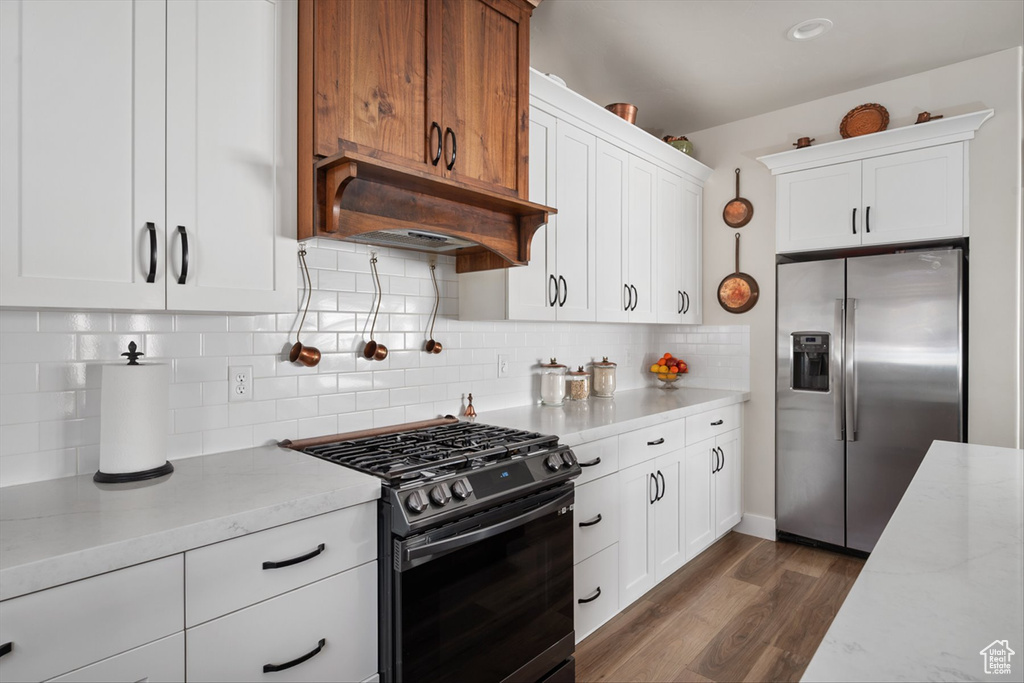 Kitchen with tasteful backsplash, appliances with stainless steel finishes, dark wood-style flooring, light stone counters, and under cabinet range hood