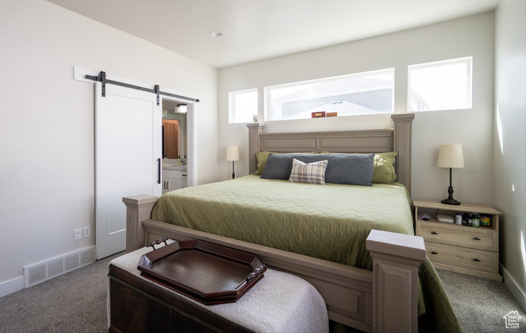 Carpeted bedroom featuring a barn door, visible vents, baseboards, and ensuite bathroom