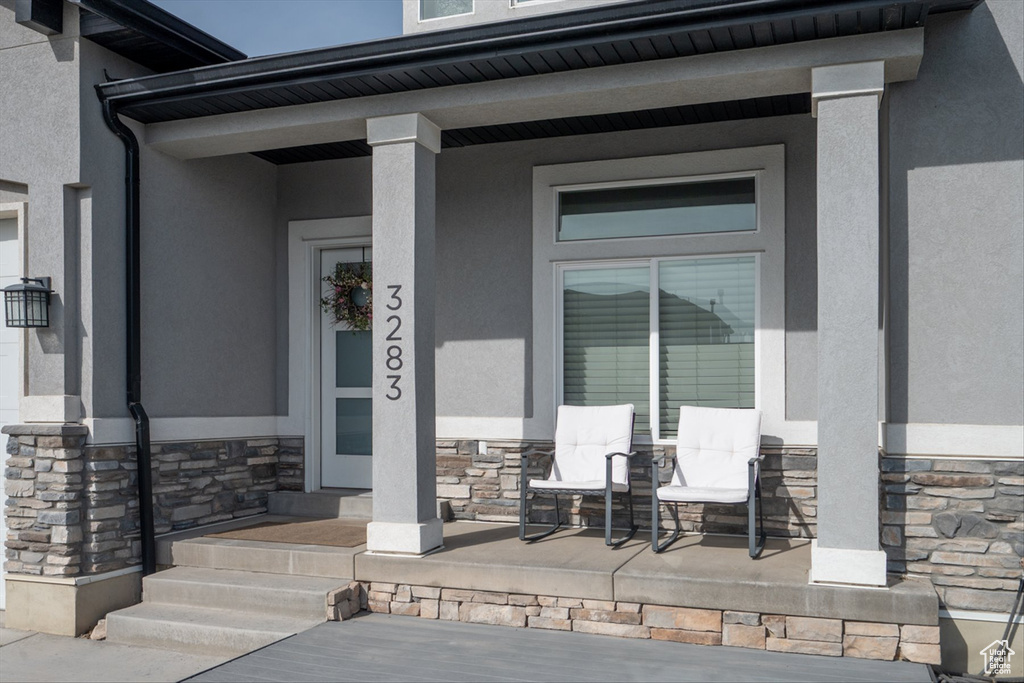 Doorway to property with covered porch, stucco siding, and stone siding