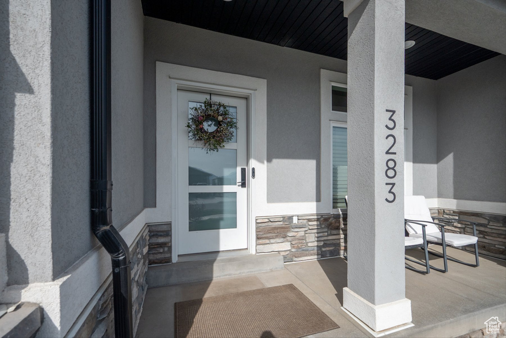 Doorway to property with a porch, stucco siding, and stone siding