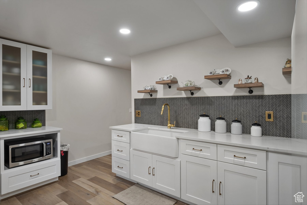 Kitchen with open shelves, a sink, stainless steel microwave, white cabinetry, and light wood finished floors