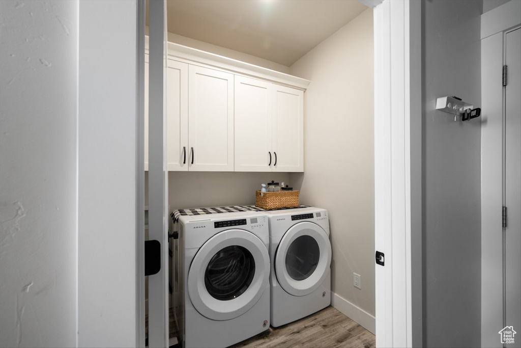Laundry room with washing machine and dryer, baseboards, light wood-style flooring, and cabinet space