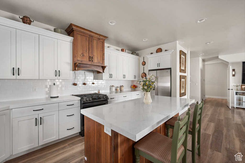 Kitchen with tasteful backsplash, freestanding refrigerator, gas range, under cabinet range hood, and wood finished floors