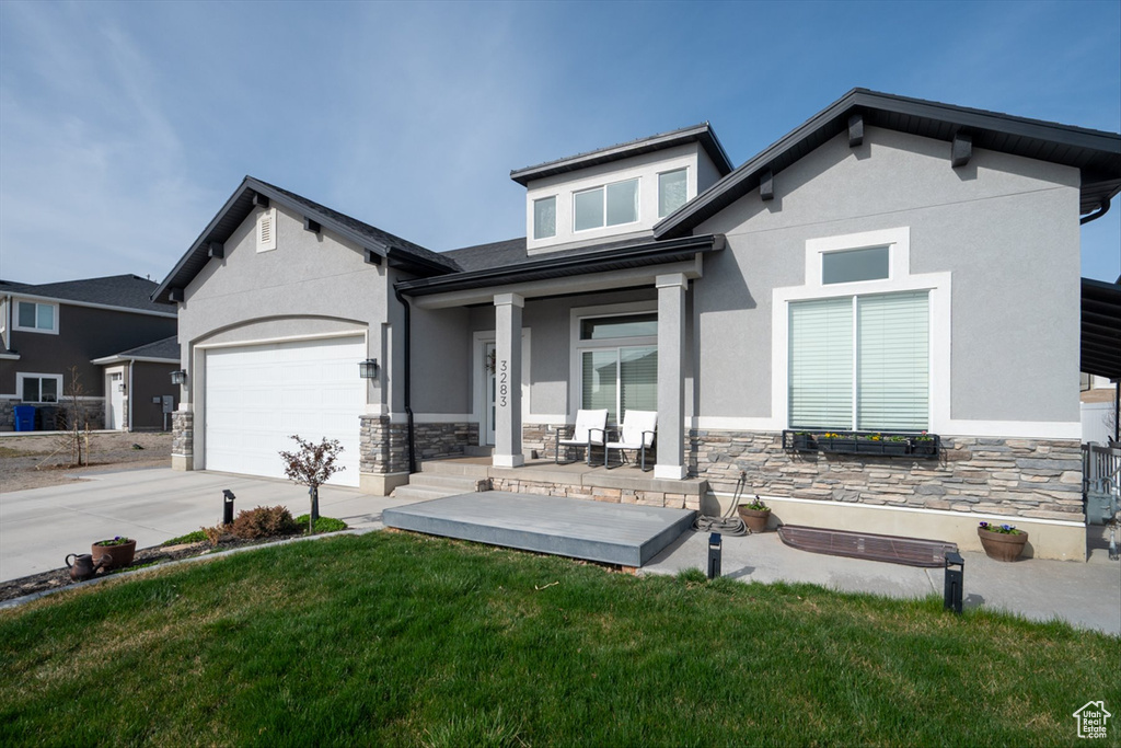 View of front of house with a garage, stucco siding, stone siding, a front lawn, and driveway