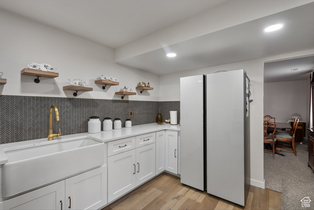 Kitchen featuring light wood-style floors, tasteful backsplash, white cabinetry, open shelves, and a sink
